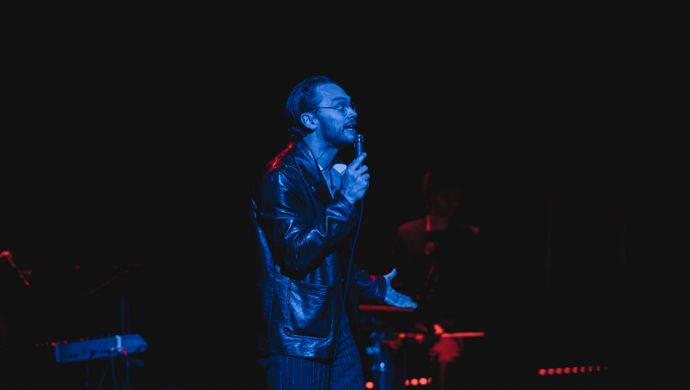 Singing Sean Nicholas Savage and drummer in blue and red light.