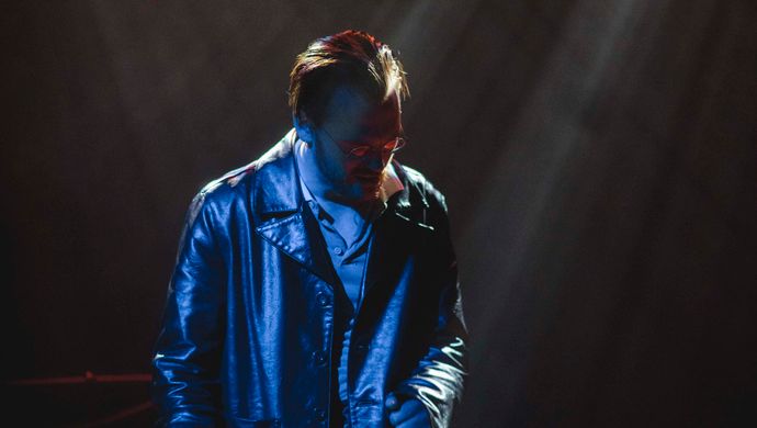 Sean Nicholas Savage singing and bathed in blue light, with a white spotlight in the background