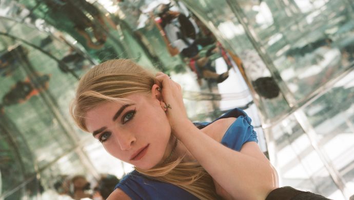 Kelly Moran, blonde vrouw met rode lipstick, zit in een spiegelruimte