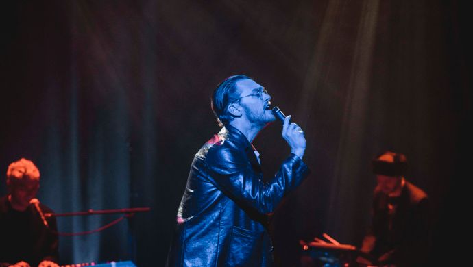 Singing Sean Nicholas Savage, keyboardist and drummer in blue and red light.