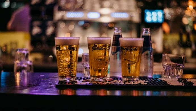 A tray with three freshly poured beers sits on the bar during Disco Royale at de Doelen. The background is blurred, featuring colorful light reflections and a lively bar atmosphere.