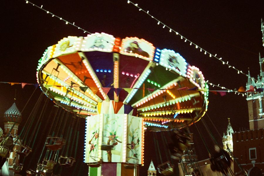 Verlichte zweefmolen op een kermis tijdens de avond, omringd door lichtslingers en historische gebouwen op de achtergrond.