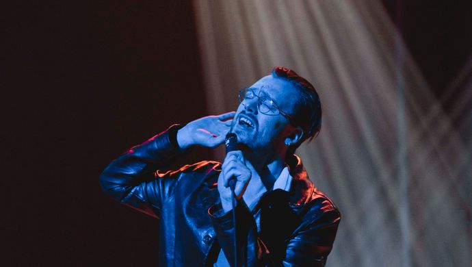 Sean Nicholas Savage singing and bathed in blue light, with a white spotlight in the background