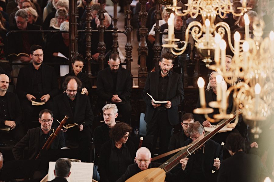Muziekensemble gekleed in het zwart voert een concert uit in een rijk versierde kerk, omringd door barokke ornamenten en gouden details.