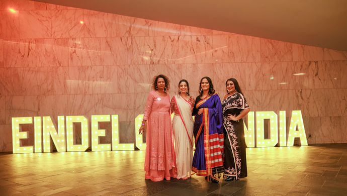 Drie vrouwen voor lampen die ''Eindeloos India'' spellen