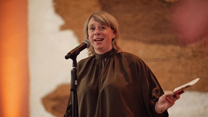 Vrouw in een bruin shirt praat voor een microfoon
