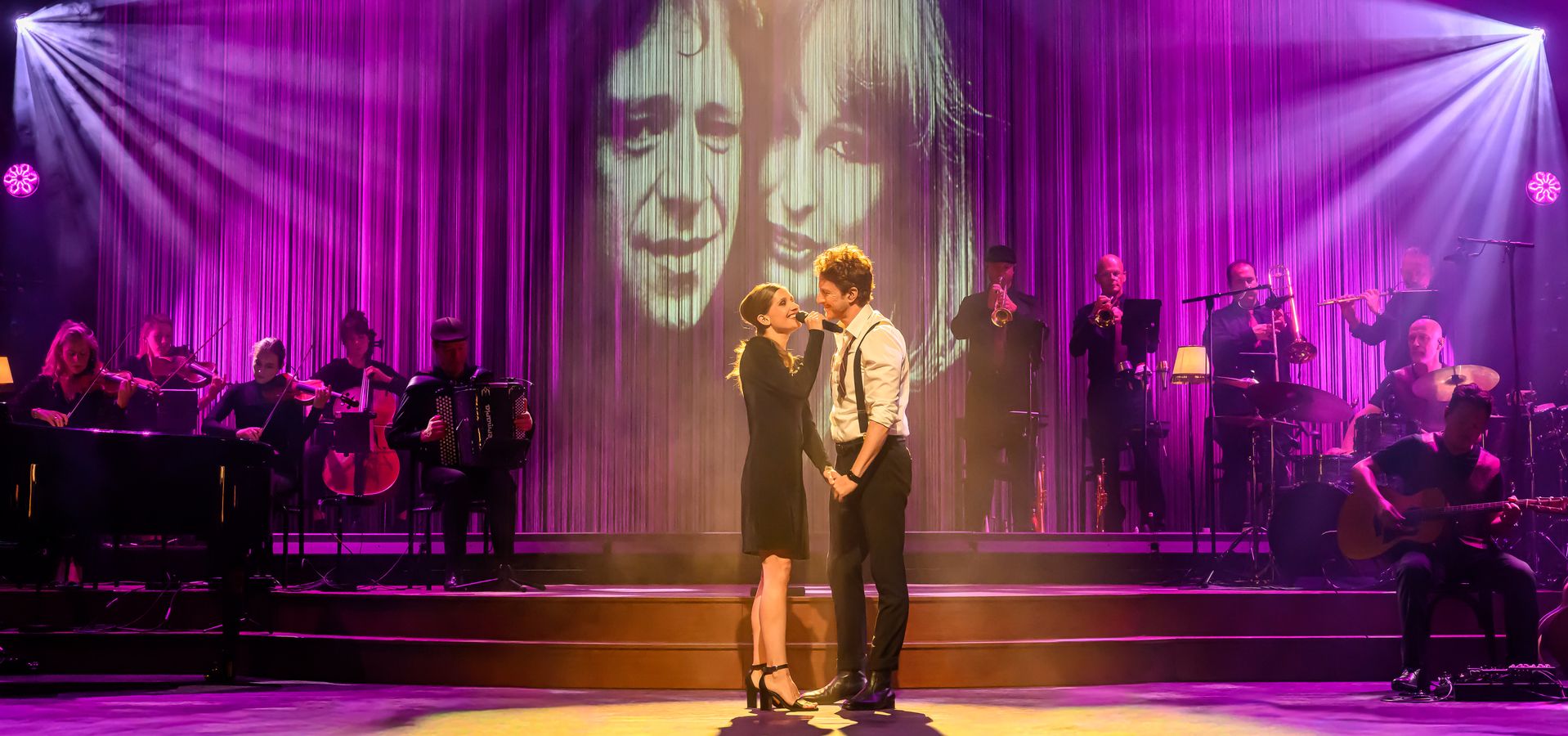 vrouw en een man aan het optreden op een podium met een live band en paarse podium verlichting