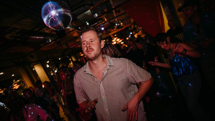 A man dances beneath a disco ball during Disco Royale at de Doelen. The colorful lights, reflections, and other people dancing in the background contribute to the energetic and festive atmosphere.