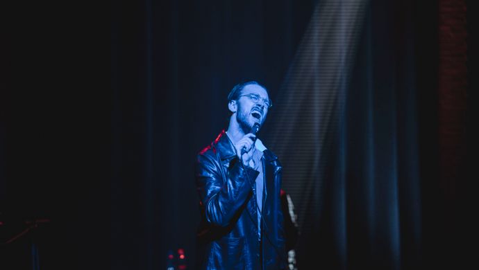 Sean Nicholas Savage singing and bathed in blue light, with a white spotlight in the background