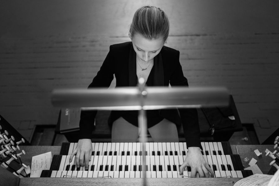 Zwart-witfoto van een organist die geconcentreerd speelt op een pijporgel. De persoon buigt zich licht voorover, met beide handen op het toetsenbord en het gezicht gericht naar beneden, gefocust op de muziek.