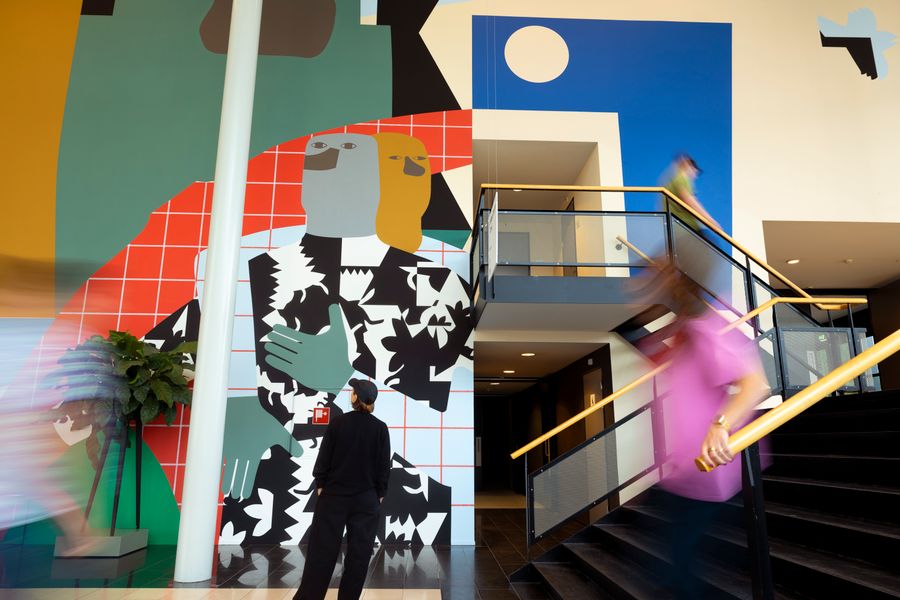 Bezoeker bekijkt een groot, kleurrijk muurschilderwerk in de Doelen terwijl andere bezoekers voorbijlopen tijdens de Art Walks-kunstroute.