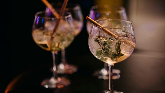 Three gin and tonic glasses with ice, mint, and straws sit on a glossy table during Disco Royale at de Doelen. Colorful light reflections on the glass and tabletop enhance the festive atmosphere.