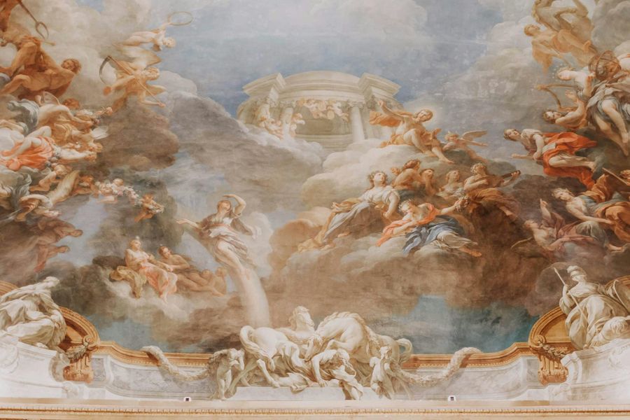 Barok plafondschildering met engelen, goddelijke figuren en dramatische wolkenpartijen in warme tinten, omlijst door rijkelijk versierde gouden ornamenten.