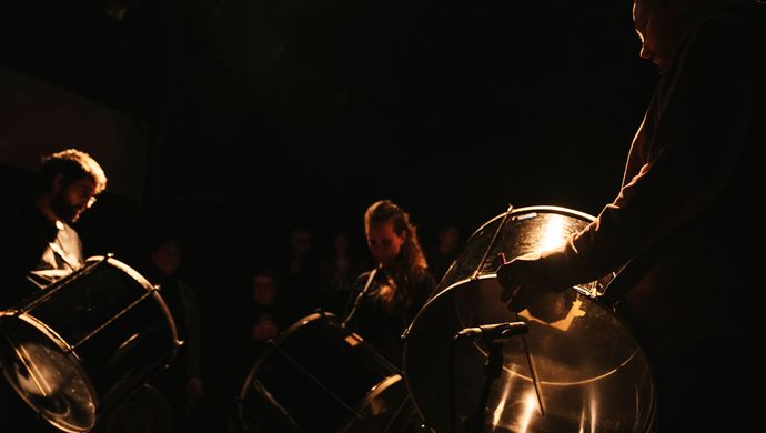 Muzikanten spelen koperblazers tijdens een optreden in een donkere ruimte, verlicht door warm, sfeervol licht dat reflecteert op de instrumenten.