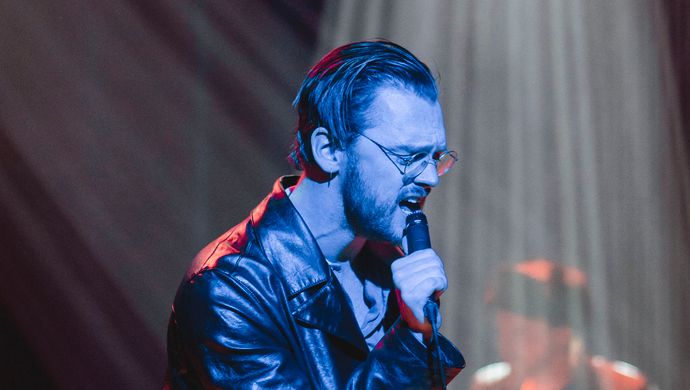 Sean Nicholas Savage singing and bathed in blue light, with a white spotlight in the background