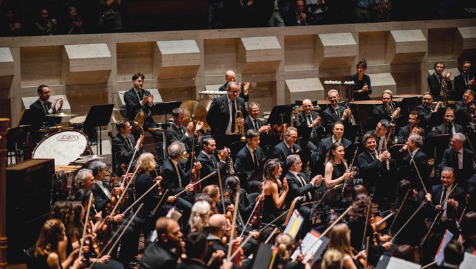 Orkestleden applaudiseren en kijken naar elkaar 