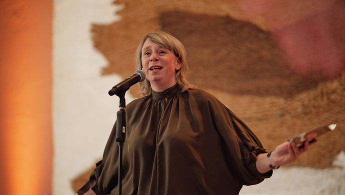 Vrouw in een bruin shirt praat voor een microfoon