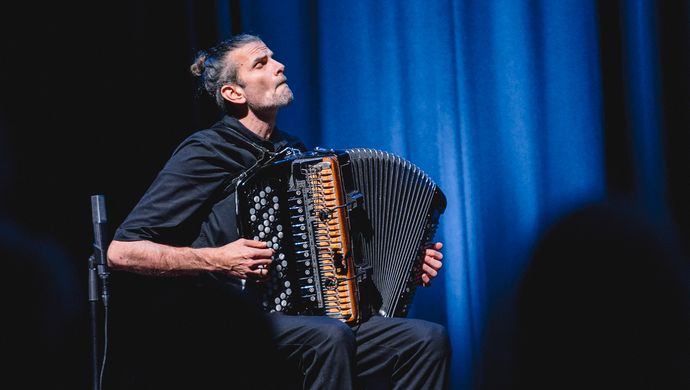 Accordeonist speelt op het podium in een intieme, blauw verlichte setting. 