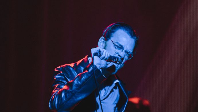 Singing Sean Nicholas Savage and drummer in blue and red light.
