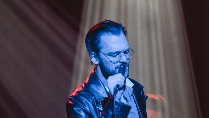 Sean Nicholas Savage singing and bathed in blue light, with a white spotlight in the background