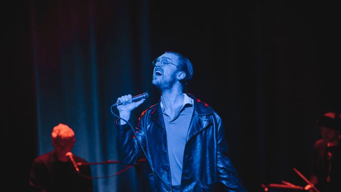 Singing Sean Nicholas Savage, keyboardist and drummer in blue and red light.