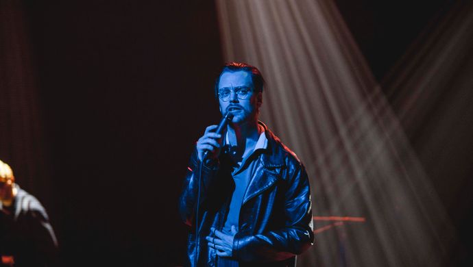 Sean Nicholas Savage singing and bathed in blue light, with a white spotlight in the background